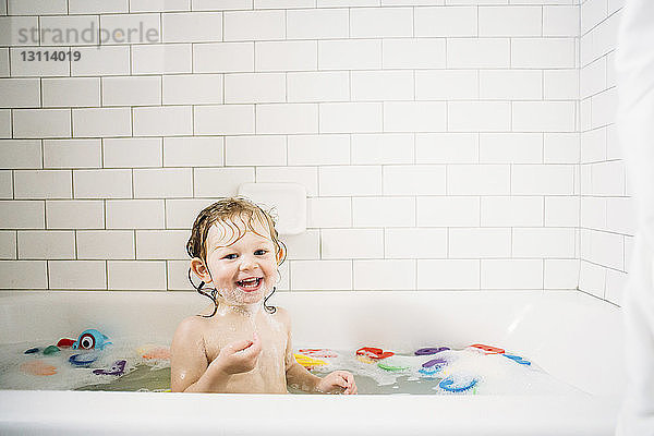 Porträt eines fröhlichen Mädchens  das in einer Badewanne vor einer gefliesten Wand badet