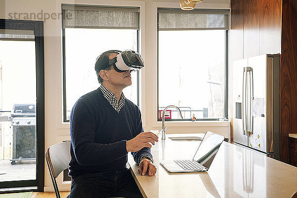 Mann trägt einen Virtual-Reality-Simulator und sitzt am Tisch in der Küche