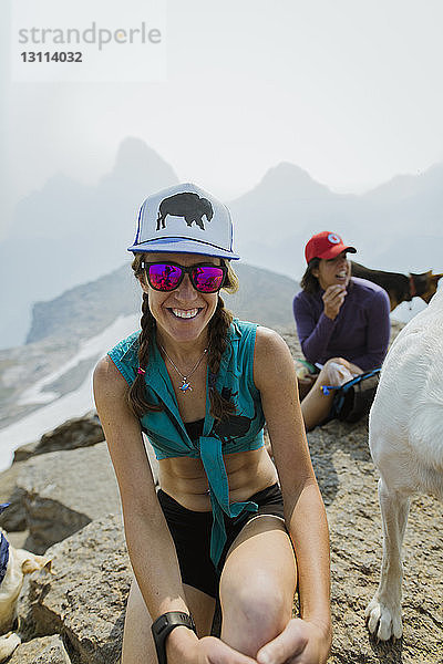 Weibliche Wandererinnen mit Hund sitzen auf Berg gegen klaren Himmel
