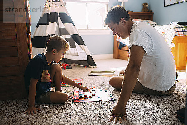 Vater und Sohn spielen Dame  während sie zu Hause auf einem Teppich sitzen