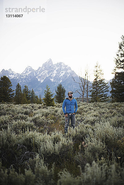 Wanderer mit Händen in den Taschen auf dem Feld gegen Berge und klaren Himmel im Grand-Teton-Nationalpark stehend