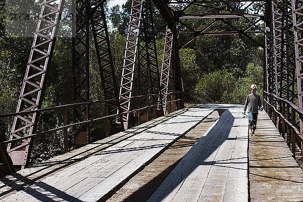 Frontansicht eines Jungen mit Angelruten beim Gehen auf der Brücke bei Sonnenschein