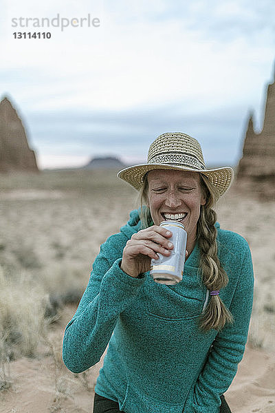 Fröhliche Wanderin mit Hut beim Trinken in der Wüste