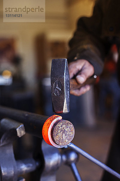 Beschnittenes Bild eines Handwerkers  der in einer Fabrik Metall schmiedet