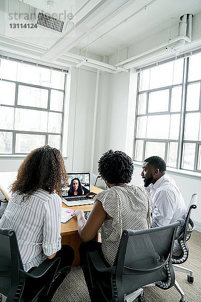 Geschäftsleute diskutieren mit Geschäftsfrau über Videokonferenz im Sitzungssaal im Büro