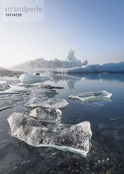 Szenerieansicht von Eisbergen mit auf dem Meer schwimmendem Eis vor klarem Himmel im Winter