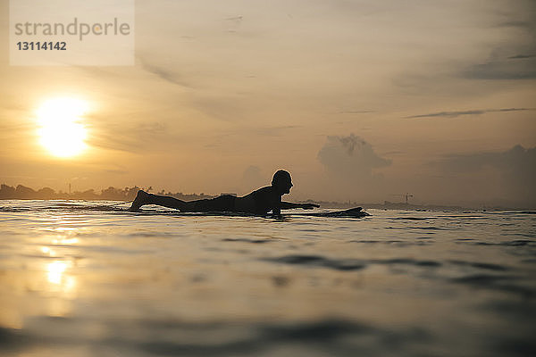Seitenansicht der Silhouette eines Mannes  der bei Sonnenuntergang auf dem Meer gegen den Himmel surft