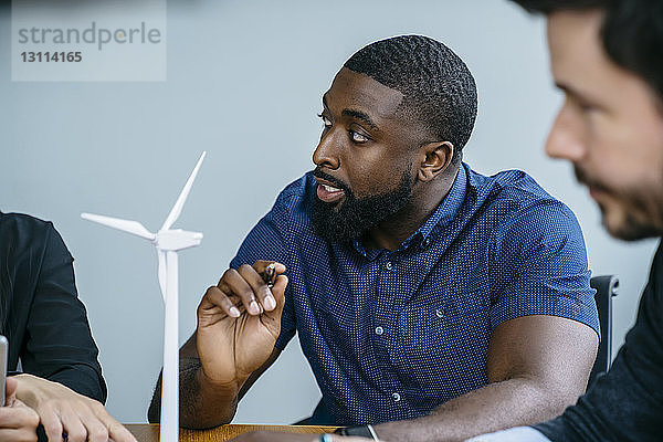 Geschäftsleute  die während einer Besprechung im Büro am Modell einer Windkraftanlage arbeiten