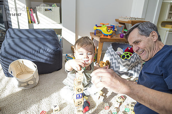 Glücklicher Großvater und Enkel spielen zu Hause im Wohnzimmer mit Spielzeugbausteinen
