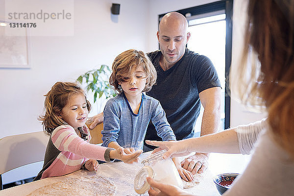 Eltern helfen Kindern beim Kneten von Teig bei Tisch in der Küche