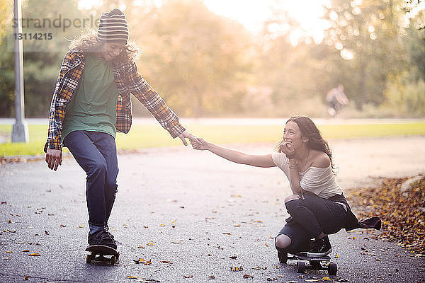 Paar hält sich beim Skateboarden auf der Straße an den Händen