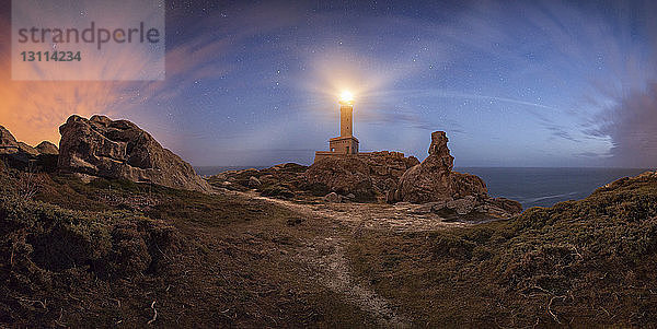 Beleuchteter Leuchtturm gegen bewölkten Himmel an der Küste während der Nacht