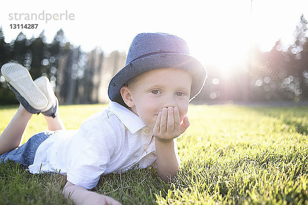 Porträt eines niedlichen Jungen  der auf einem Grasfeld im Park liegt