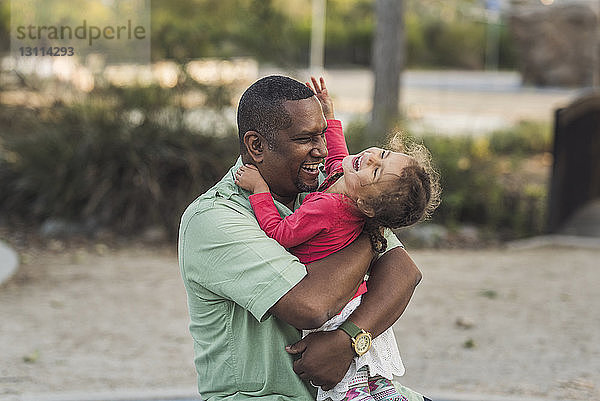 Fröhlicher Vater spielt mit niedlicher Tochter auf dem Spielplatz