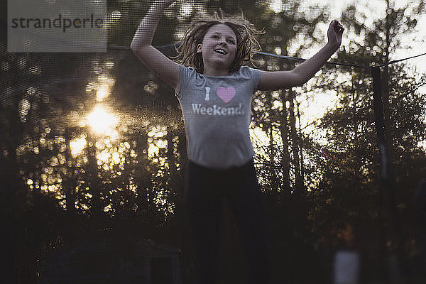 Fröhliches Mädchen springt bei Sonnenuntergang auf dem Spielplatz auf dem Trampolin