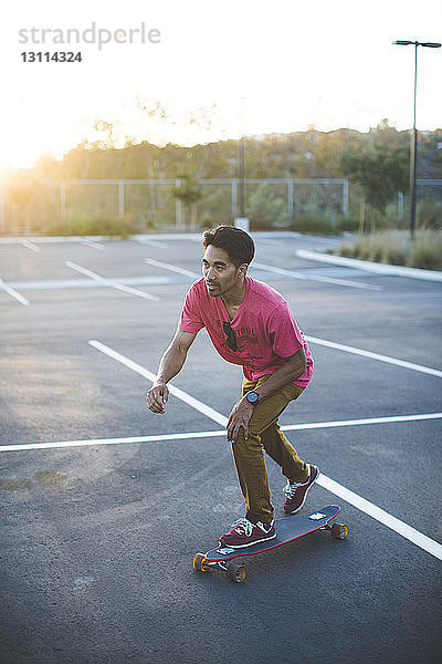 Mann fährt Skateboard auf Parkplatz bei Sonnenuntergang