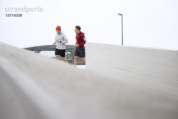 Männliche Freunde joggen auf Fußweg auf Parkplatz gegen klaren Himmel