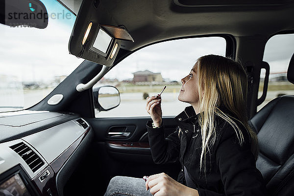 Seitenansicht eines Mädchens  das Lippenstift aufträgt  während es im Auto sitzt