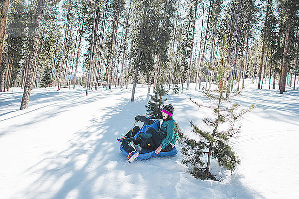 Hochwinkelaufnahme von Mutter und Sohn  die auf einem schneebedeckten Feld gegen Bäume rutschen