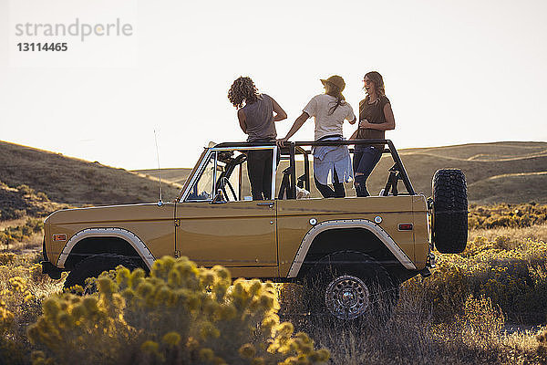 Freundinnen stehen im Geländewagen auf dem Feld gegen den klaren Himmel