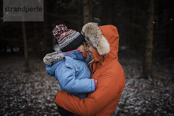 Glückliche Mutter mit Tochter im Winter im Wald stehend