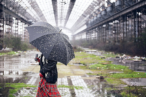 Frau mit Regenschirm geht bei Schneefall auf dem Feld