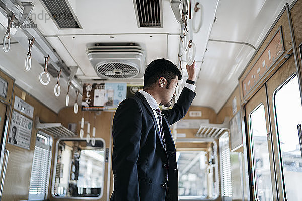 Seitenansicht eines nachdenklichen jungen Geschäftsmannes  der durch ein Fenster schaut  während er im Zug steht