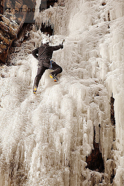 Mann klettert gefrorenen Wasserfall gegen Felsformation