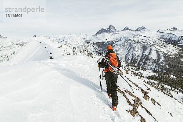 Rückansicht eines Wanderers mit Rucksack und Skistöcken beim Wandern auf einem schneebedeckten Berg