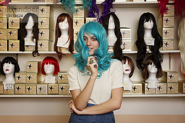 Porträt einer Frau mit blauer Perücke  die im Geschäft vor Schaufensterpuppen steht
