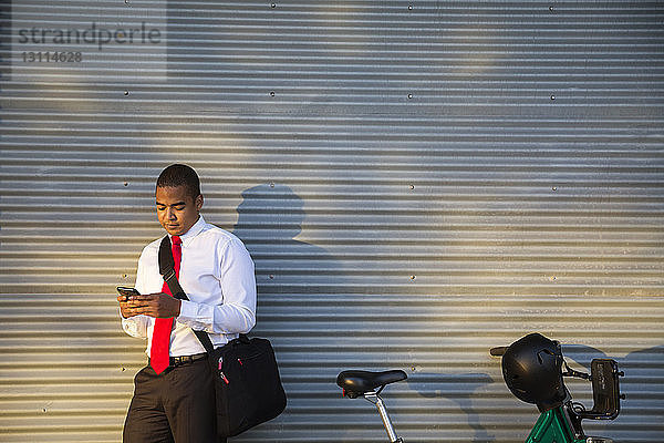 Geschäftsmann benutzt Mobiltelefon  während er gegen den geschlossenen Verschluss steht