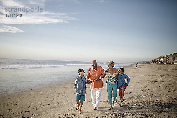 Glückliche Großeltern mit Enkeln  die am Strand gegen den Himmel laufen