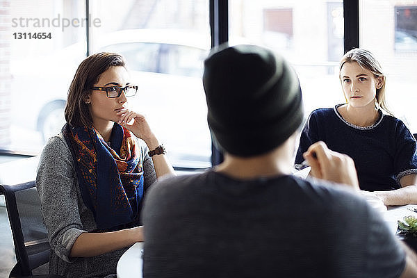 Weibliche Kollegen  die einem Geschäftsmann während einer Besprechung im Büro zuhören