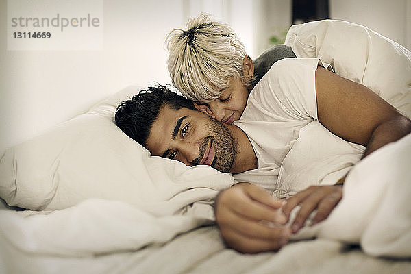 Porträt eines lächelnden Mannes  der mit einer liebenden Frau zu Hause im Bett liegt