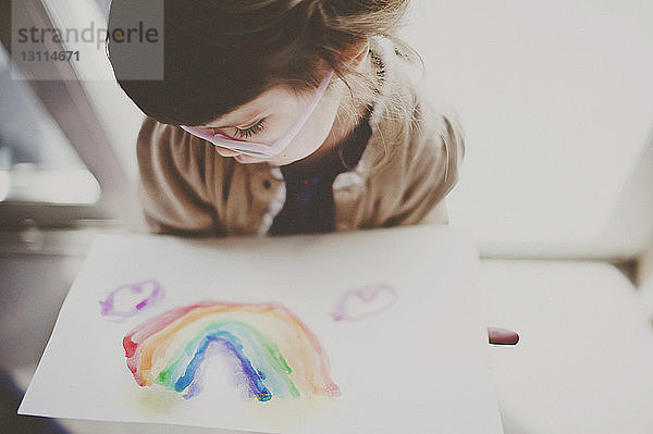 Süßes Mädchen betrachtet auf Papier gemalten Regenbogen
