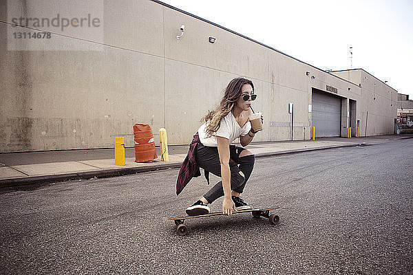 Frau trinkt Smoothie beim Skateboarden auf der Straße