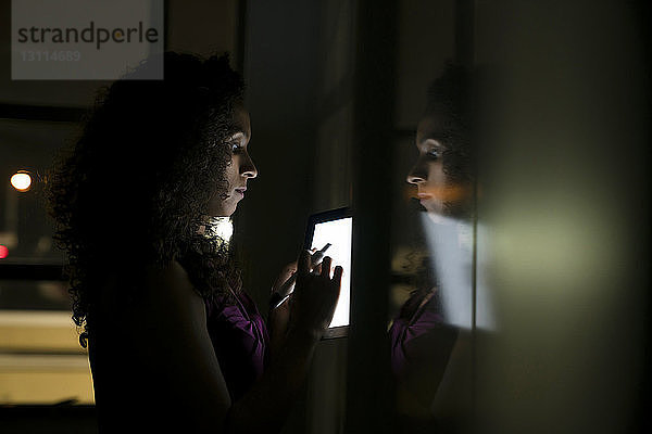 Geschäftsfrau steht am Whiteboard und benutzt Tablet-Computer in dunklem Büro