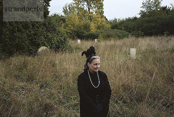 Traurige Frau schaut weg  während sie auf dem Friedhof steht