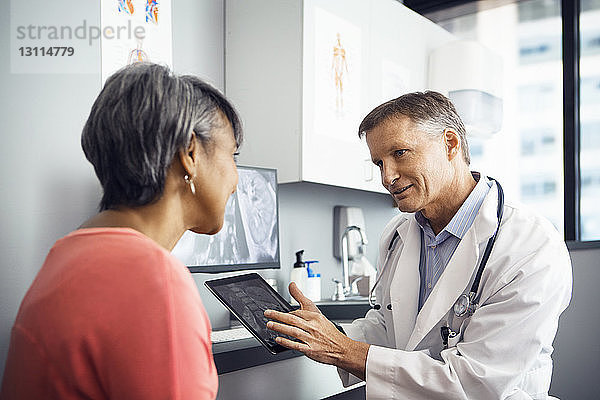 Männlicher Arzt erklärt dem Patienten in der Klinik das Röntgenbild am Tablet-Computer