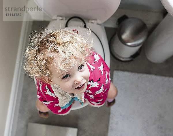 Porträt eines glücklichen Mädchens  das auf der Toilette im Badezimmer sitzt