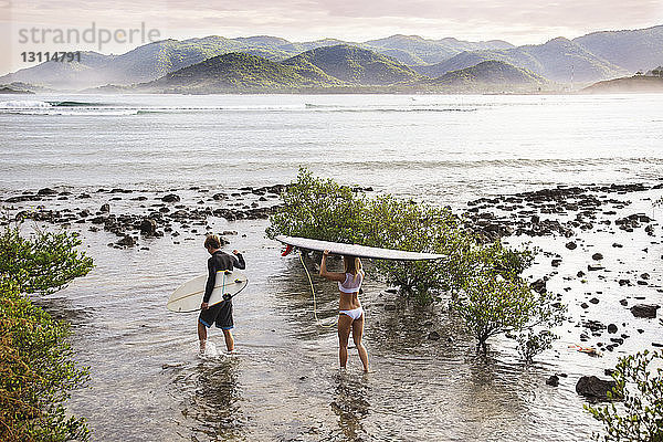 Hochwinkelansicht von Surfern  die Surfbretter tragen  während sie auf das Meer zugehen