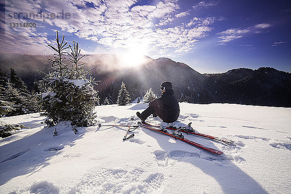Skifahrer schaut auf Aussicht  während er auf verschneitem Berg sitzt