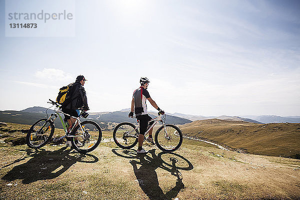 Freunde stehen mit Fahrrädern auf Berg gegen Himmel