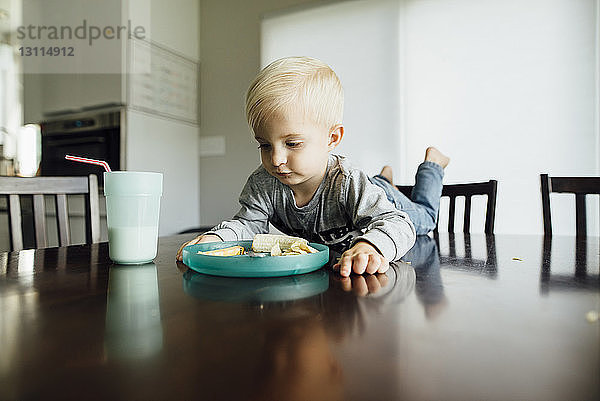 Kleiner Junge isst zu Hause auf dem Tisch liegend