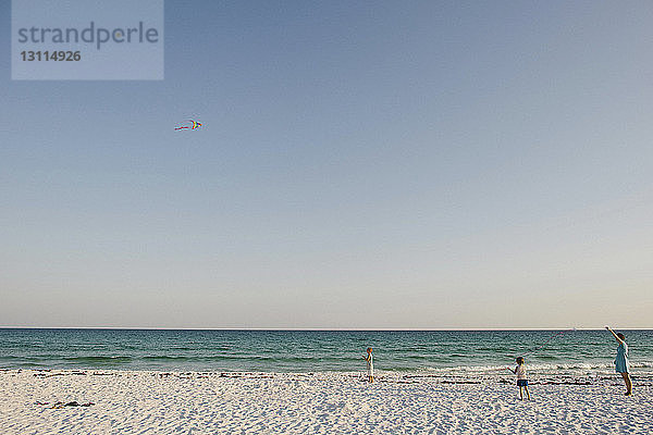 Familie fliegt Drachen am Strand gegen klaren Himmel