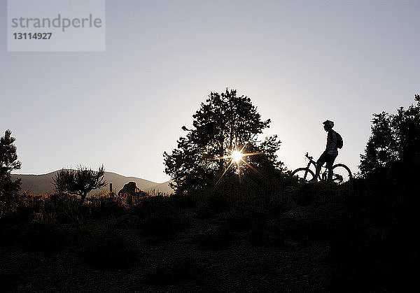 Scherenschnitt eines Mannes mit Fahrrad auf dem Feld vor klarem Himmel bei Sonnenuntergang