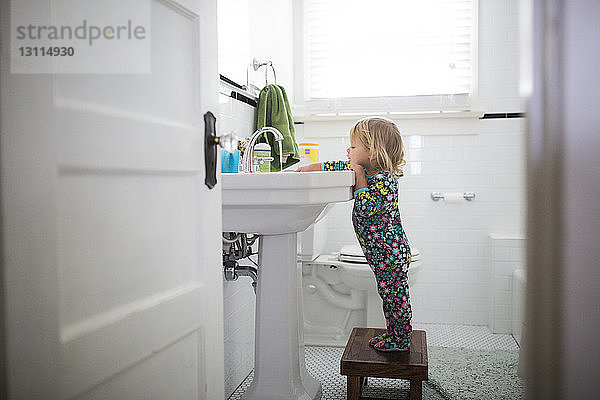 Seitenansicht eines auf einem Hocker stehenden Mädchens am Waschbecken im Badezimmer