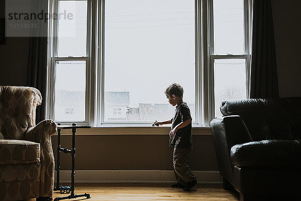 Seitenansicht eines Jungen  der zu Hause auf dem Fensterbrett mit einem Spielzeugmotorrad spielt