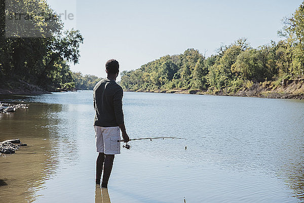 Rückansicht eines Mannes  der eine Angelrute hält  während er im See vor klarem Himmel steht