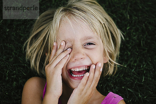 Portrait eines glücklichen Mädchens  das sich im Gras liegend die Augen reibt